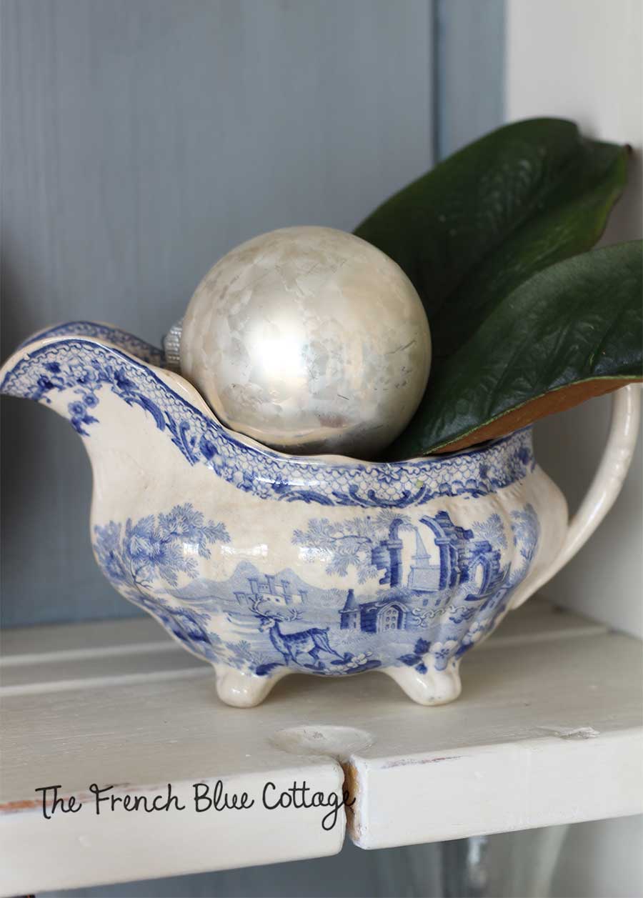 Blue and white gravy boat with vintage ornament and magnolia.