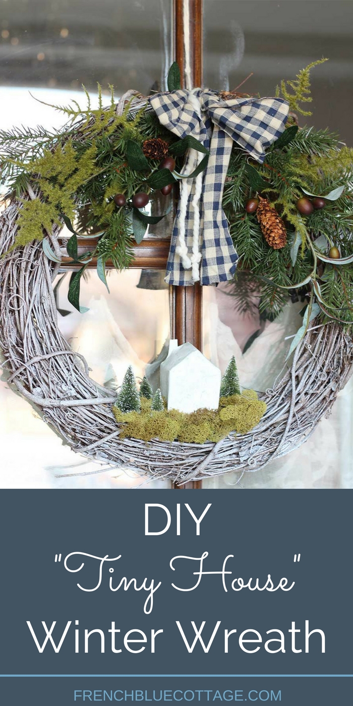A DIY winter wreath with a paper mâché house and bottle brush trees.
