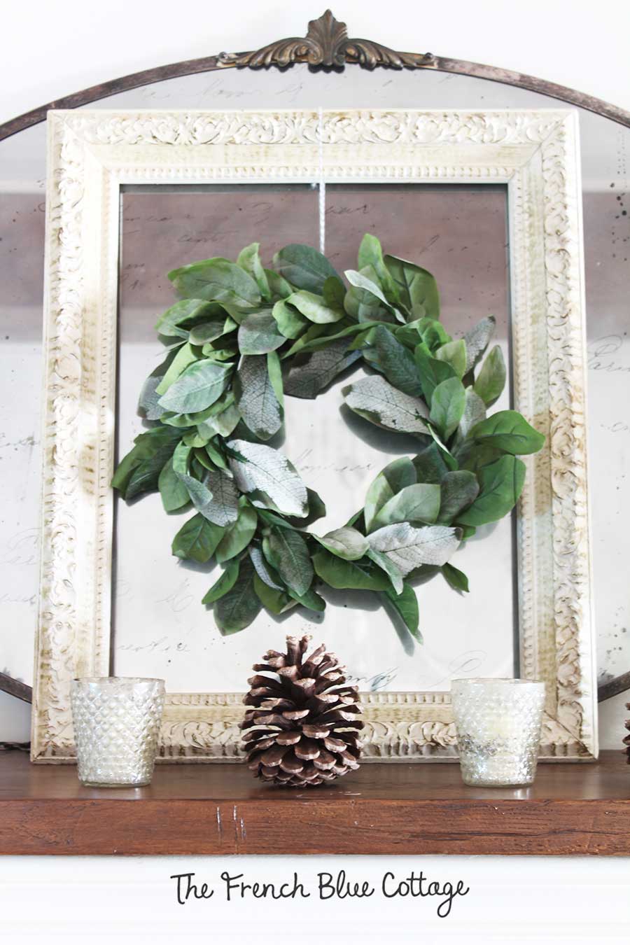 Pinecones on a winter mantel with a layered wreath, frame, and mirror.