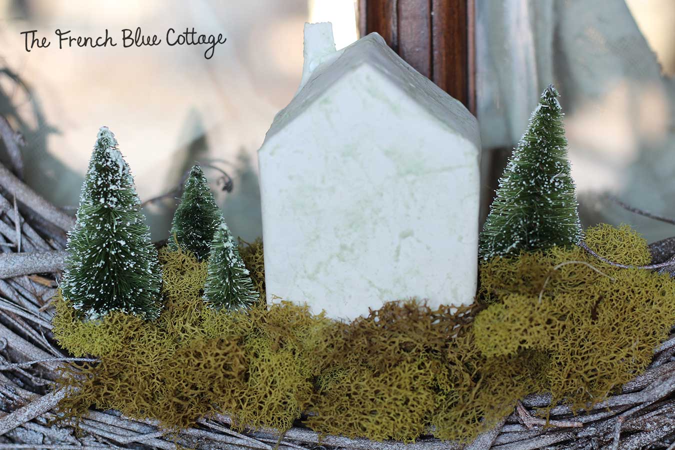 Tiny paper mâché house and bottle brush trees in a wreath.
