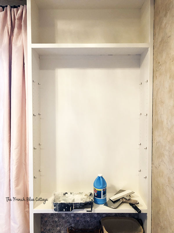 white bookshelf preparing for a starched fabric wallpaper treatment