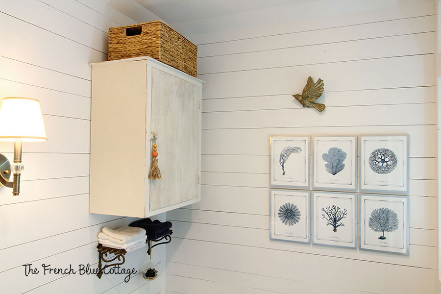 coastal farmhouse bathroom with chippy cabinet, tassel, and seagrass basket