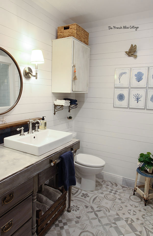 coastal farmhouse bathroom with chippy cabinet, round mirror, and sea fan art