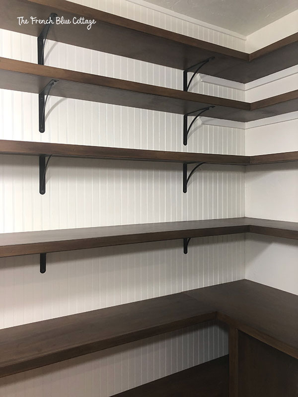 pantry under stairs with beadboard, stained shelves, and black shelf brackets