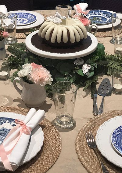 how to decorate a round table with greenery, blue and white plates, seagrass placemats, and silk butterflies