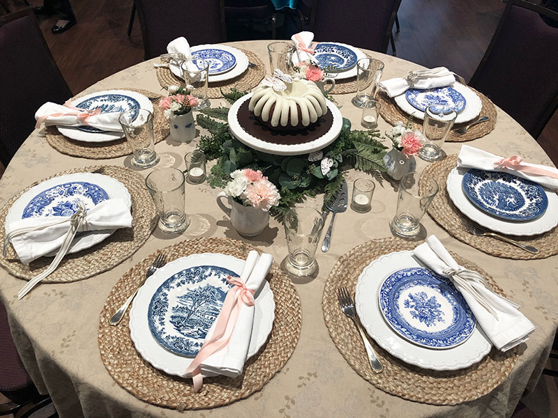 round table centerpiece ideas for decorating, blue and white plates, seagrass placemats, bundt cake on a stand in the center