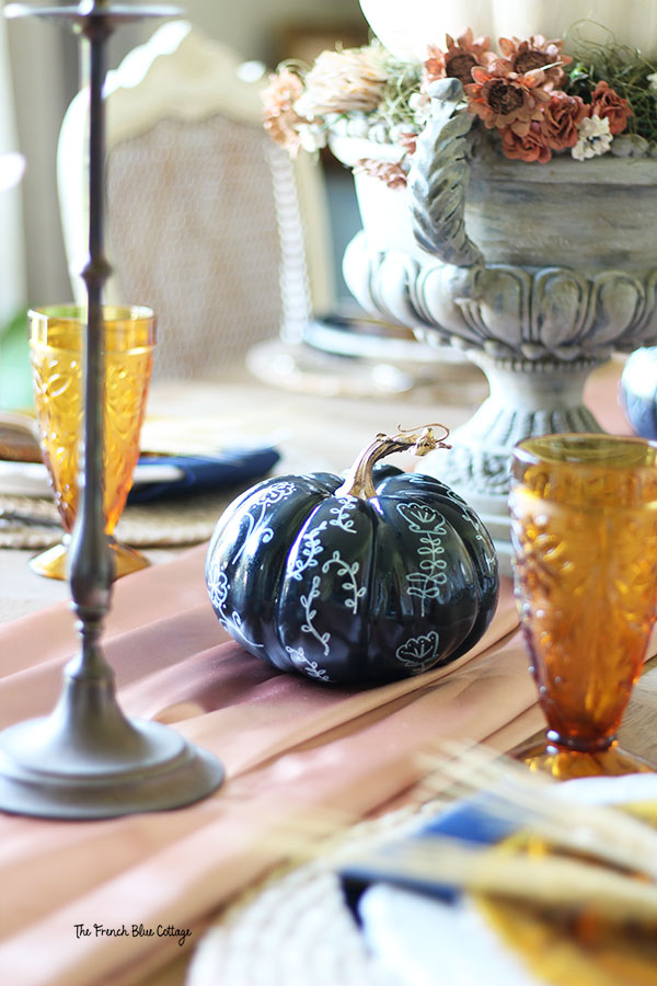 fall table decor with a navy painted pumpkin that has white paint pen designs and a gold painted stem