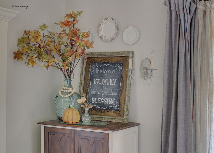 fall vignette with a chalkboard in an ornate frame, a glass vase with tall autumn branches, and a vase with a single, gold painted stem