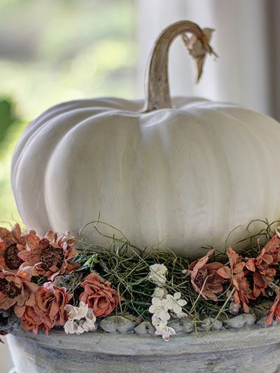 plaster flowers that look dried surround a faux white pumpkin on a gray painted urn
