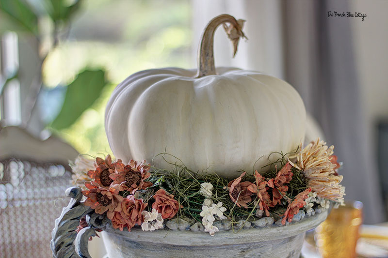 plaster flowers that look dried surround a faux white pumpkin on a gray painted urn