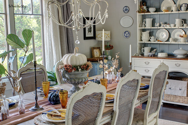 dining table set for fall with a blue and white china hutch in the background