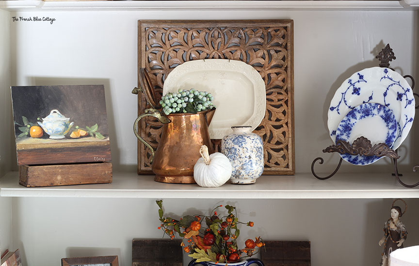 fall decor on bookshelf with copper teapot and an oil painting