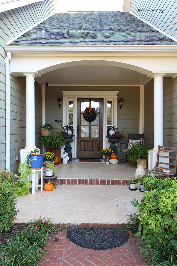 front porch decorated for fall with ferns, pumpkins, and yellow mums