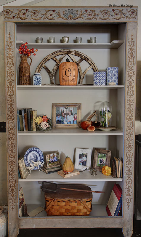 fall decor on bookshelf with ceramic pumpkin with initial, leaves, and velvet pumpkins