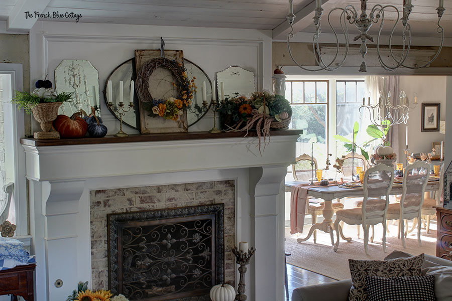 white mantel with fall decor including a basket of flowers, pumpkins, and a wreath