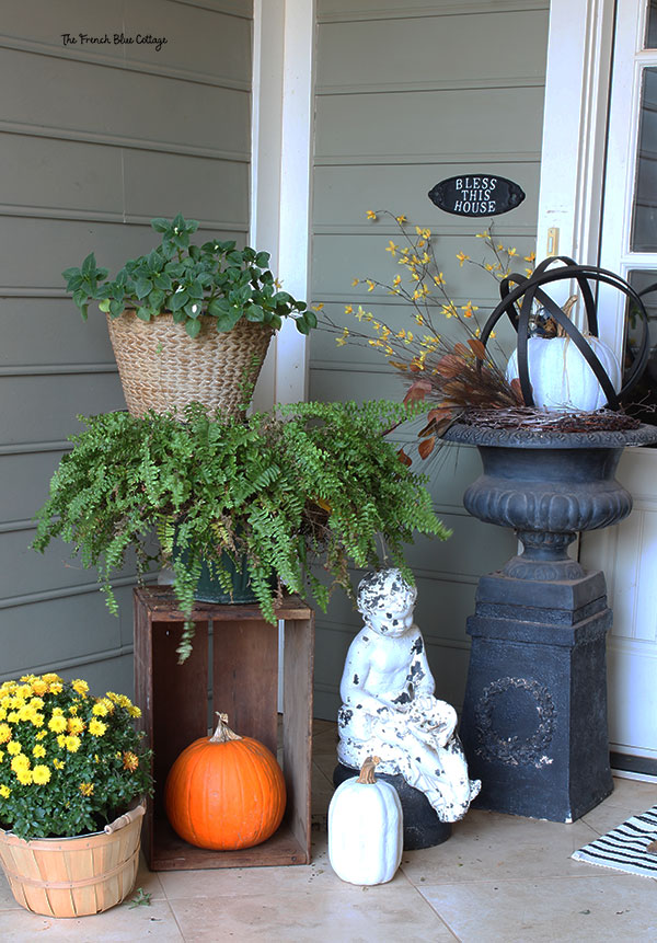 fall porch vignette with a crate with a fern on top, pumpkin inside, and small white statue