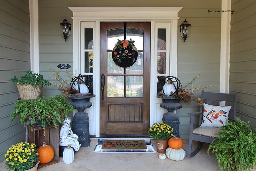 fall decor on the front porch including pumpkins, yellow mums, and ferns